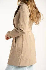Trench impermeable de corte oversize en color camel, con diseño de doble botonadura, solapas clásicas y cinturón ajustable en la cintura.