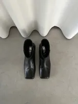 Botas de caña corta de cuero negro, con puntera cuadrada, taco bajo y cierre lateral interno.