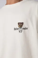 Remera de corte oversize color gris oscuro, confeccionada en algodón premium de alto gramaje. Presenta un diseño minimalista con un pequeño estampado frontal que incluye un oso y el texto 'Richer & Louder VCP'.