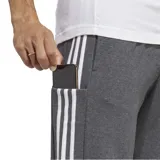 Pantalón de jogging gris con cintura elástica ajustable con cordón, bolsillos laterales y puños acanalados. Diseño con tres rayas blancas verticales a los costados y logo de Adidas bordado en blanco.