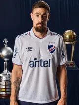 Camiseta de fútbol Umbro del Club Nacional de Football, modelo Home 2026. Diseño blanco con tejido jacquard que presenta un patrón sutil de copas históricas. Incluye cuello en V con detalles en azul y rojo, logo de Umbro, escudo del club y sponsor Antel en el frente.