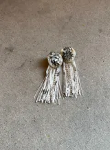 Caravanas colgantes con base circular decorada con cristales y piedras, y flecos largos de hilo blanco combinados con cadenas de strass.