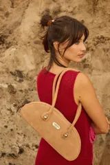 Cartera estilo baguette de cuero con silueta alargada y compacta, diseñada para llevar bajo el brazo. Presenta manijas largas con detalles de nudos esféricos metálicos en las uniones.