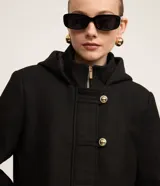 Saco corto negro de polivelour con capucha, cuello alto con cremallera, abotonado delantero cruzado, bolsillos delanteros y mangas largas.