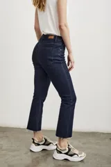 Pantalón de jean azul oscuro, de tiro medio, corte ajustado en las piernas y acampanado desde la rodilla hasta el tobillo. El ruedo es desflecado.