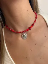 Gargantilla corta de cuentas rojas de diferentes tamaños y formas, con dije colgante plateado con diseño abstracto.