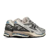 Championes New Balance modelo 1906, de estilo running urbano, con diseño técnico en tonos gris, plata y detalles en azul marino. Presenta una estructura de malla transpirable con refuerzos sintéticos, logo N lateral y entresuela con tecnología de amortiguación.