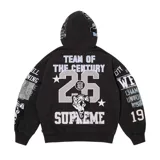 Campera con capucha y cierre frontal completo, confeccionada en algodón negro. Presenta múltiples aplicaciones gráficas bordadas y estampadas en el frente, mangas y capucha, con motivos deportivos y tipografía estilo varsity.