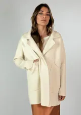 Saco tejido color crudo, con cuello solapa, mangas largas con puños acanalados y bolsillos delanteros de parche.