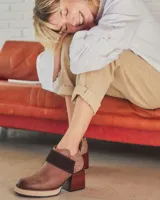 Botinetas de cuero con diseño combinado. Presentan puntera y lateral en cuero liso marrón, una banda central en gamuza oscura y talón con textura de reptil. Incluyen plataforma y taco cuadrado de madera, con cierre lateral.