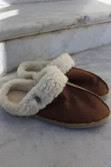 Pantufla de cuero color habano con interior de piel sintética, suela de goma y detalle de costura central.