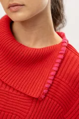Capa tipo poncho tejido de punto en algodón color rojo con cuello alto y aberturas laterales con lazos rosados.