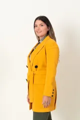 Chaqueta cruzada color mostaza con lazo y botones negros. Tiene bolsillos con tapa y detalle de cuatro botones en las mangas.