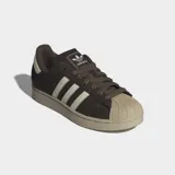 Championes Adidas Superstar II de cuero nobuk en color marrón oscuro, con las icónicas tres rayas laterales y la puntera de caucho en tono crema. Presenta una suela de caucho al tono y forro interior de felpa.