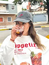 Gorro de béisbol de color gris oscuro (obsidian) con efecto lavado, confeccionado en algodón. Presenta un bordado frontal de un ají picante rojo y verde.