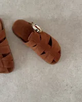 Zueco tipo sandalia de gamuza color tostado, con diseño de tiras entrelazadas y hebilla metálica decorativa en el empeine.