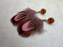 Par de aros colgantes con base redonda negra, detalles dorados y plumas negras.