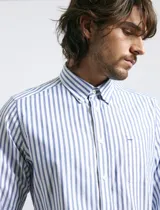 Camisa de corte clásico confeccionada en tejido oxford, con diseño de rayas verticales en tonos azul y blanco. Presenta cuello abotonado, cierre frontal con botones y bolsillo en el pecho con detalle de etiqueta bordada.