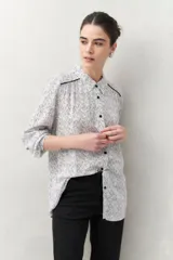 Camisa de manga larga confeccionada en 100% viscosa, color blanco con estampado de rayas finas negras. Presenta cuello camisero, botones frontales negros y detalles de ribete negro en los hombros.