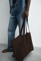 Bolso tipo shopper de gran tamaño confeccionado en piel con acabado de serraje. Presenta un diseño minimalista con costuras visibles, compartimento principal amplio y dos asas de hombro integradas.