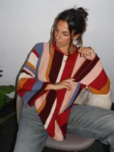 Sweater tejido a mano con terminaciones en crochet, de silueta oversize y mangas acampanadas. Presenta un diseño de rayas verticales multicolores en tonos tierra, rojo, azul y crema.
