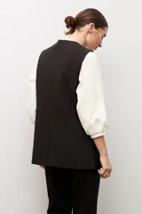 Chaleco largo sastrero de color negro, con escote en V profundo, cierre frontal con un botón metálico y bolsillos laterales con solapa.
