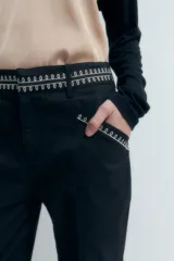 Pantalón negro de corte recto con bolsillos laterales y bordado en contraste blanco en cintura y bolsillos.