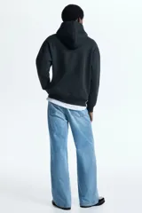 Canguro negro H&M con capucha, bolsillo frontal tipo canguro y diseño gráfico de Fender en el pecho.