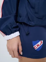 Campera deportiva Umbro del Club Nacional de Football, modelo Sky para mujer. Diseño en tonos azul marino y celeste con detalles en blanco y líneas finas rosadas, cuello alto, cierre frontal y bolsillos.