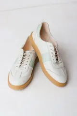 Zapatilla de cuero color crudo con detalle de una franja lateral en verde agua y cordones color beige.