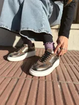 Zapatillas deportivas de cuero color peltre, con cordones negros y suela de goma blanca.