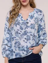 Blusa holgada de rayón y poliéster, marca Zac & Rachel, con estampado floral en tonos azules sobre fondo blanco. Posee escote en V con muesca central, mangas largas abullonadas con inserción de puntilla y puños elastizados.