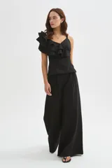 Blusa negra de poliéster con cuello en V, tirantes anchos y un diseño asimétrico con volados escalonados en un hombro. Corte entallado.