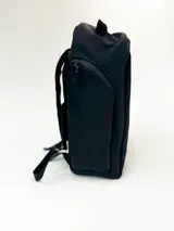 Mochila de color verde oliva con paneles en tonos de verde contrastantes y detalles en negro. Presenta un bolsillo frontal con cierre y un pequeño parche rectangular con texto en la parte inferior.