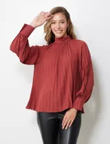 Blusa color ladrillo de gasa plisada con cuello alto, manga larga abullonada con puño y botón de ajuste. Espalda con abertura ojal y doble abotonadura.