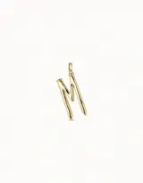 Dije con forma de letra M, bañado en oro, con diseño inspirado en un clavo. Pieza artesanal de estilo minimalista.