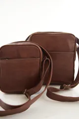 Morral bandolera de cuero genuino color marrón, con diseño compacto, cierre superior y correa ajustable para el hombro.