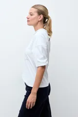 Remera blanca de manga tres cuartos, con cuello redondo y detalles de bordado calado en la parte frontal y hombros.