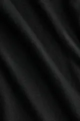 Buzo negro de punto fino, corte corto y escote asimétrico que deja un hombro al descubierto. Posee mangas largas con puños acanalados.