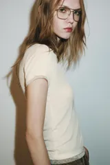 Camiseta de manga corta color marrón oscuro con textura acanalada, cuello redondo y bajo recto. Presenta un bajo superpuesto de tul o tela más clara, visible en el ruedo y en el cuello.