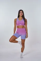 Conjunto deportivo compuesto por un top y un short de ciclismo, ambos con diseño degradado que transiciona de fucsia a lila. El top presenta cuello redondo y logo 'bk.' estampado en el frente, mientras que el short es de tiro alto y ajuste ceñido.