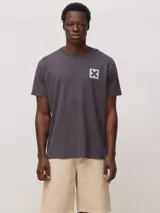 Camiseta de algodón orgánico color gris oscuro, con corte regular fit y cuello redondo. Presenta un pequeño estampado cuadrado con una cruz en el pecho.