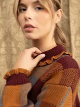 Campera de punto con diseño a cuadros tartán en tonos marrones y beige. Presenta un corte oversize, cierre frontal con cremallera, cuello tipo babero con volados y mangas largas con puños ajustados.