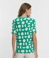 Blusa de viscosa con cuello redondo, manga corta y diseño con nudo lateral. Presenta un estampado geométrico de semicírculos blancos sobre fondo verde.