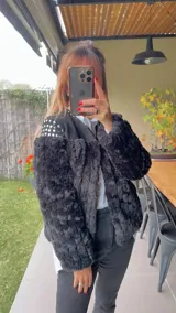 Chaqueta corta de piel sintética blanca con interior de gamuza negra y apliques de tachas plateadas y doradas en la espalda.