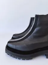 Botas negras de cuero con caña baja, cierre lateral con cremallera y suela track.