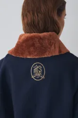 Campera bomber de paño color azul marino, con cuello de piel sintética en color marrón desmontable, cierre frontal y puños elásticos. Presenta logo bordado en el frente y bolsillos laterales.
