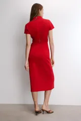 Vestido midi de color rojo, con cuello solapa, manga corta y cierre frontal de botones metálicos. Presenta bolsillos decorativos en el pecho y un cinturón a tono en la cintura.