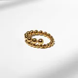 Anillo dorado de acero con diseño de borlas macizas de tamaño decreciente que se cruzan en el frente.