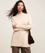Suéter de punto color crema, con cuello alto, mangas largas y botones decorativos en los puños.